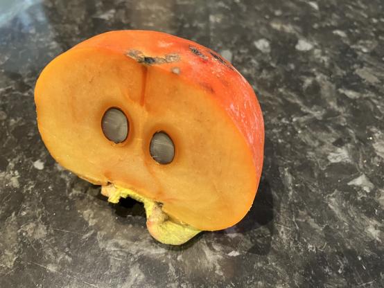 A persimmon has been sliced in half, revealing two seeds that look like eyes