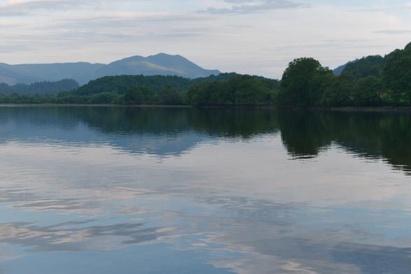 clouds, trees and mountain reflected in calm water of a loch