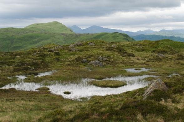 small lochan, green mountains in light and shadow with clouds