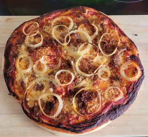 Eine Pizza auf einem Holzbrett. Es sind Zwiebelringe auf der Pizza zu erkennen.