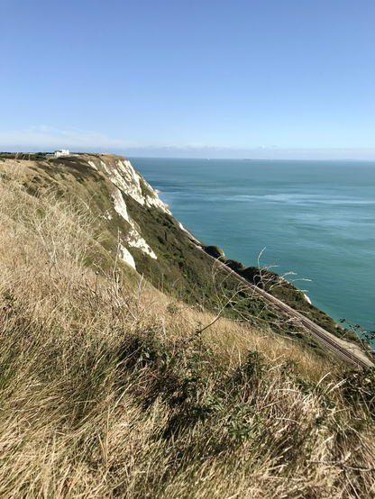 Seitlicher Blick auf Kreideklippen, links Steilhang mit Gras, im Hintergrund der Ärmelkanal in Türkis