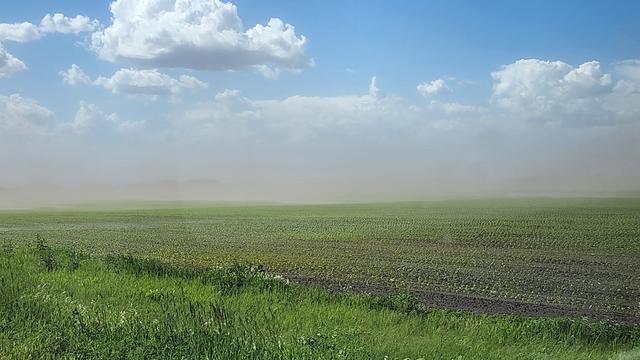White clouds float over farmers green field, with brown haze hanging in the middle.
