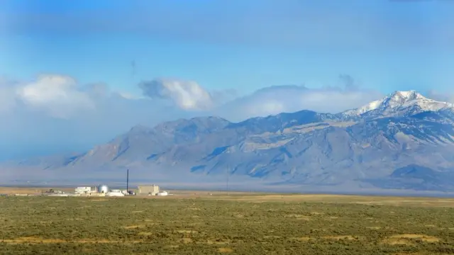 photo of a lonely industrial facility in a flat landscape with tall mountains in the background