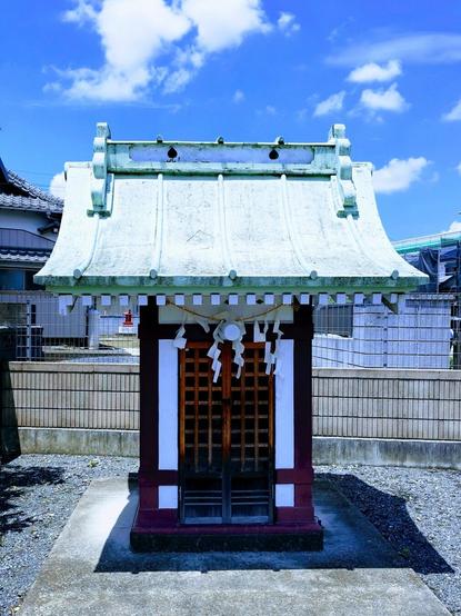 A tiny shrine among some residential housing.  The photo's colors have been edited to highlight its turquoise roof. Everything contrasts nicely with the mostly blue sky.