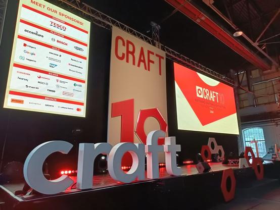 Nahaufnahme der Bühne der Craft Conference. Die Bühne ist dekoriert mit roten und weißen Elementen und dem Schriftzug "craft" in weiß. Im Hintergrund ist ein Screen mit den Sponsoren der Konferenz zu sehen.