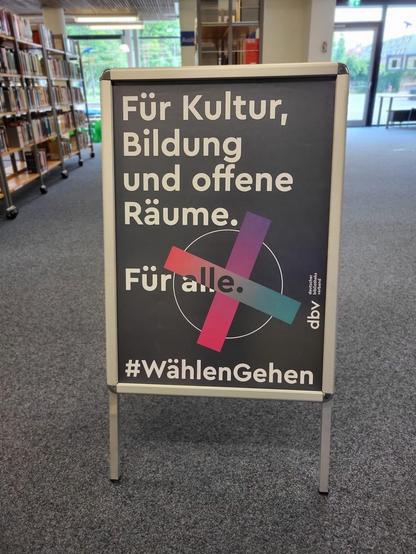 Blick in eine Bibliothek.
Auf einem Aufsteller steht: 
"Für Kultur Bildung und offene Räume-
Für alle.
#Wählen Gehen.