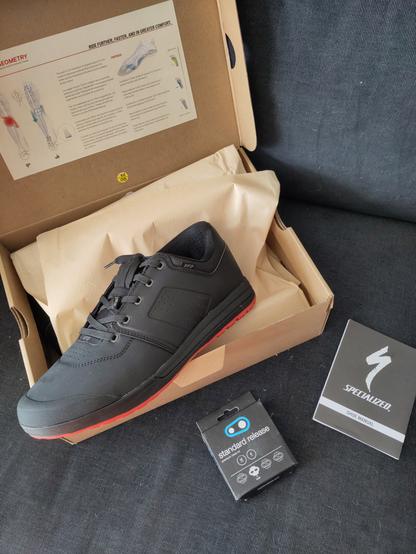 Chaussure noire à semelle rouge posée sur la boîte ouverte