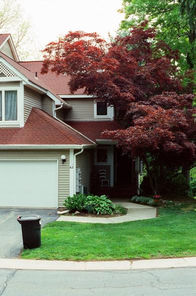 A condo with a red roof and a trash can in front of it flanked on the right by a red Japanese maple tree.