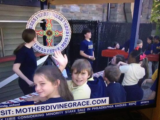 photo taken from tv of elementary age kids betting on a wheel of fortune at their church school "Italian Festival" A boy looks at camera and waves. A little girl has a knowing smirk