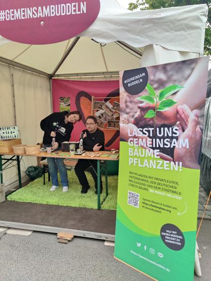 Der #GemeinsamBuddeln-Stand beim HanseKulturFestival an der Lübecker Untertrave. Zu sehen sind 2 fröhliche Mitglieder, die den Stand betreuen.