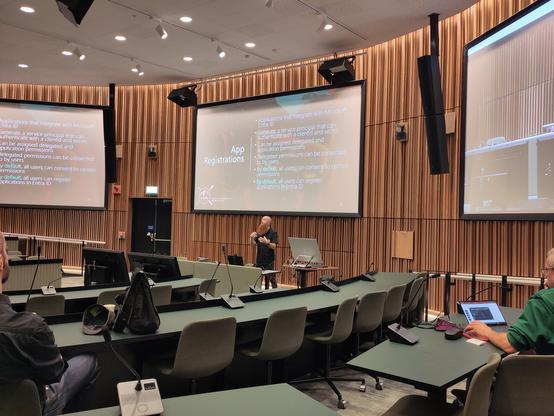 Bearded dude presenting in a cool auditorium with three screens.