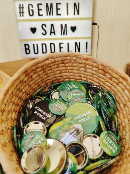 Ein Korb mit grünen Buttons, auf denen „#GemeinsamBuddeln“ steht.