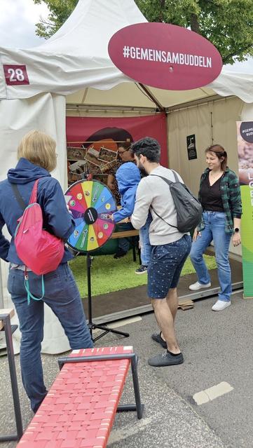 Eine Szene am #GemeinsamBuddeln-Stand beim HanseKulturFestival. Ein Mann hält ein Kind im Arm, das am Glücksrad dreht, um einen Preis zu gewinnen.