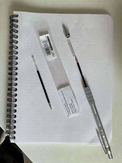 An opened Pro Mecha pen by Otho, screwed apart and two ink replacements. Laying on a Rhodia notepad with dot grid.