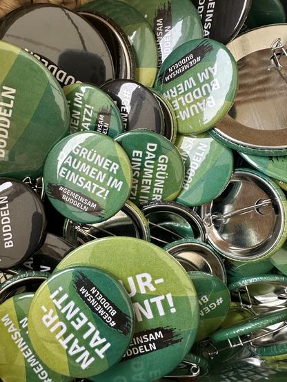 Ein Korb voller grüner Buttons, auf denen #GemeinsamBuddeln steht.