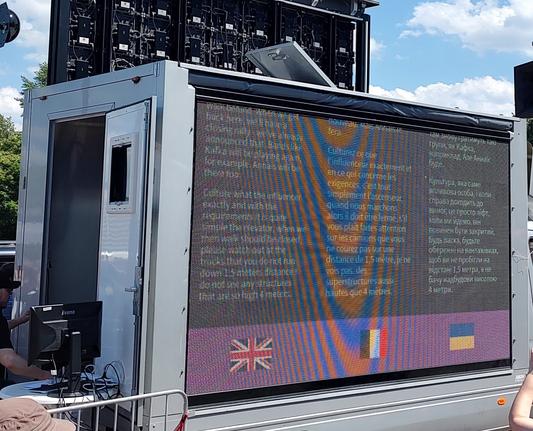 Auf einem Bildschirm werden Beiträge live in Englisch, Französisch und Ukrainisch übersetzt angezeigt.