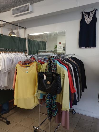 a black purse hangs on the front of a rack of clothing in a store