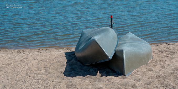 Two canoes lay upside down on the sand next to a lake.