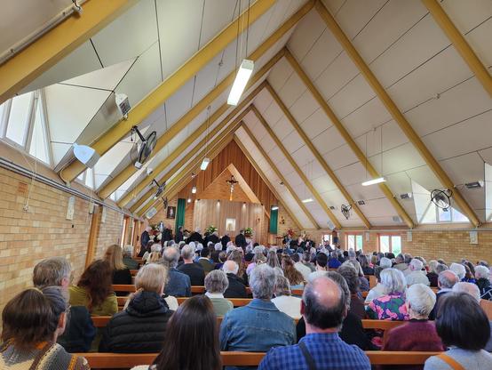 Interior of A frame mid century modern church, lots of full pews, a gospel choir and a small jazz band up at the front in the distance.