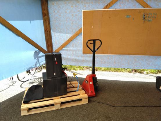 Eine Palette mit Aktivboxen auf Hubwagen unter dem Einlasszelt