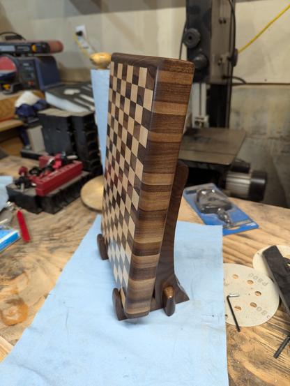 A checkered end grain cutting board of walnut and maple on a custom walnut stand in a messy garage