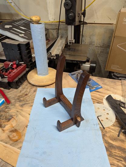 A walnut stand for the cutting board on a blue paper towel in a messy garage