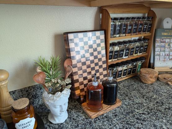 The cutting board being displayed on a kitchen counter next to spices, oils, and various olive wood decorations