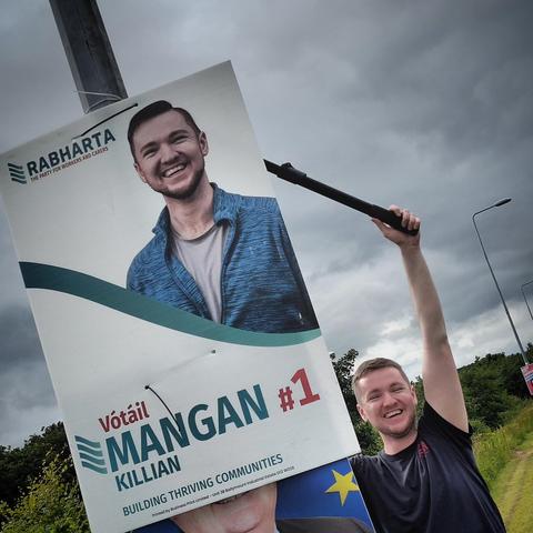 A photo of Killian holding an extendable shears cutting down his poster.