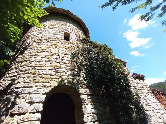 Vue en contre-plongée sur une tourelle et le début d'une muraille crénelée qui plonge vers la vallée.
Ciel bleu à peine nuageux.