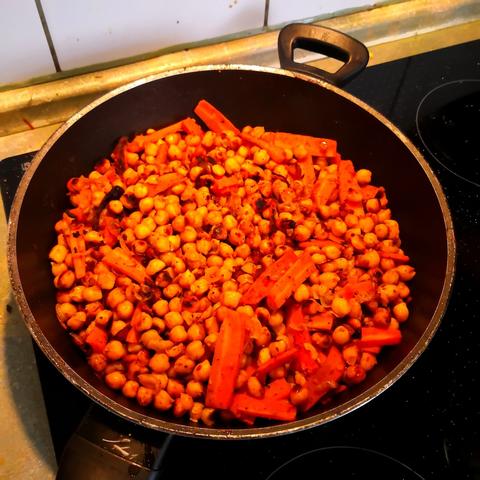 eine rötlich gewürzte Pfanne mit angebratenen Kichererbsen, dazwischen ebenfalls angebratene Karottensticks