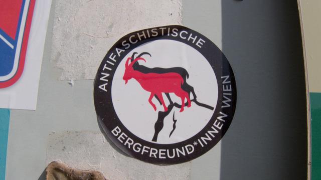 An antifa sticker on a wall. The black and red flags are replaced by goats on a mountain and the rim reads "Antifaschistische Bergfreund*innen Wien"