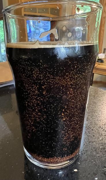 Close up of a pint glass of beer with a universe of brown sediment floating inside