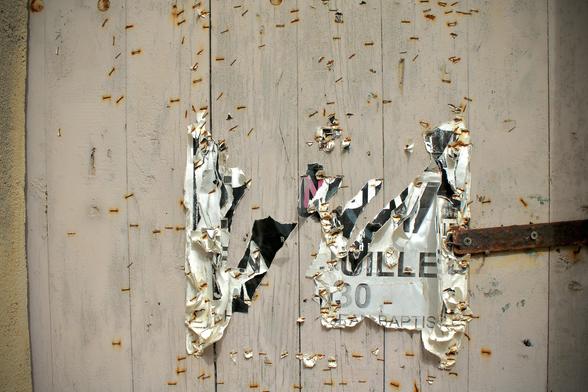 deutsch: eine nahaufnahme einer holztür oder eines hölzernen fensterladens irgendwo auf korsika zeigt die wenigen überreste und fetzen eines plakates. dadurch wird auf dem hell gestrichenen holz der blick freigegeben auf zahlreiche verrostete tackerspuren vergangener anschläge.

english: a close-up of a wooden door or shutter somewhere in corsica shows the few remnants and scraps of a poster. this reveals numerous rusty staple marks from past posters on the brightly painted wood.