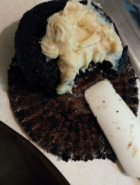 A cupcake with a big bite out of it sits on a counter with a spatula very close to it.