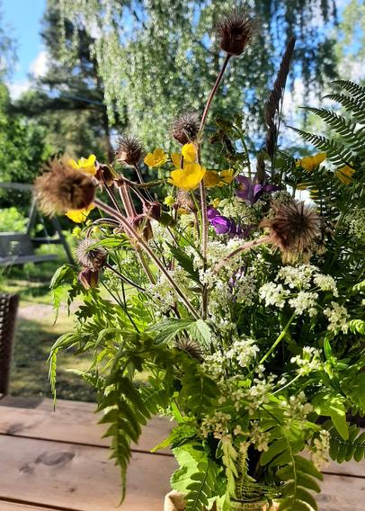 A bouquet of wild flowers in a vase on an outdoor table with the sun shining through them.
