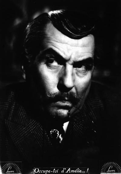 The image features a man who appears to be in the midst of an intense or dramatic scene. He is looking off to his right with a serious expression on his face, which suggests that he might be deep in thought or reacting to something unexpected. The man has a mustache and wears glasses, adding to the character's serious demeanor. There are also some additional details visible such as what seems like a book or document held near him, possibly indicating a professional or intellectual role. The style of the image suggests that it might be from an older film, given the quality and composition that is characteristic of cinema from certain eras.