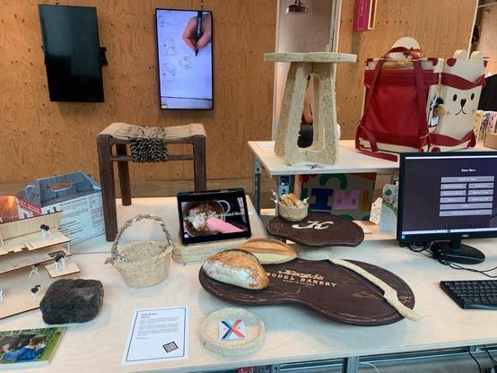 A selection of products made using the material, including stools, bucket, and dish. Other CSM exhibits are to the side and back, mounted on plywood walls.