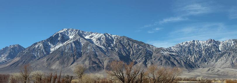 Eastern Sierras

This is a panoramic image of what is called the Eastern Sierras. This image was captured just outside of Lone Pine, California off of Highway 395.
The foreground consist of desert brush as the mountains block most clouds and storms that try to make their way over.
The gray mountains start in the distance and about half way to the top you see the snow line and to the left is the tallest peak in the lower 48 states, Mount Whitney. 
The sky is mostly clear with some thin clouds over to the right.