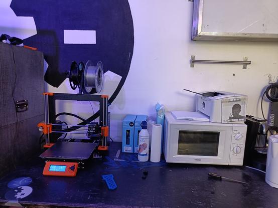 Printer and microwave oven next to a Prusa Mk3s+ 3D printer