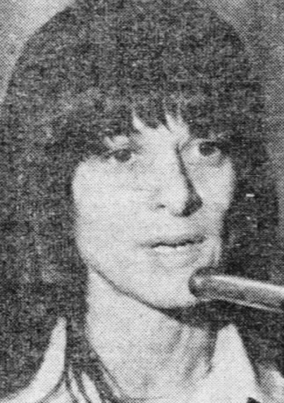Betty Santoro, from a 1978 newspaper; a woman with light skin, and dark hair cut in a shag style with bangs; speaking into a microphone