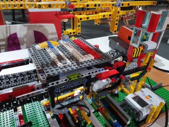 Detailfoto des LEGO-Rasterkraftmikroskop-Modells. Man sieht eine dunkelgraue LEGO-Platte (die Probe) auf der mit Steinen in verschiedenen Höhen die Buchstaben TU gesteckt wurden. Ein Motor rastert eine hellblaue Spitze über das Höhenprofil.
Man sieht rundherum ein kompliziertes Gerüst und unten rechts den Controller für die Motoren.