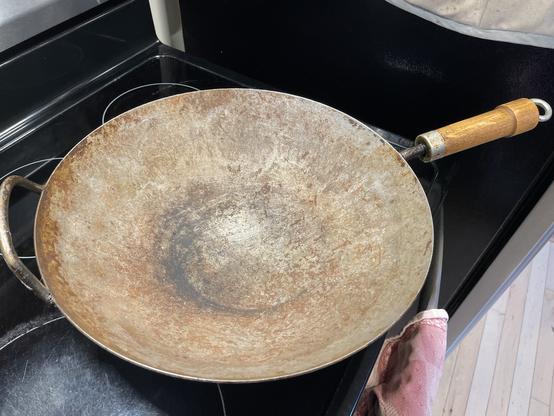 Photo of my really well-used, seasoned wok sitting on the stove (electric, unfortunately).  Lots of brown and black patches all over it, from past meals.