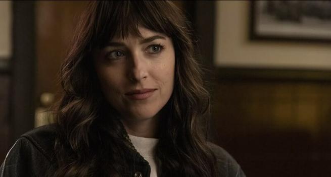 Dakota Johnson looking slightly up and to her left. She wears a dark jacket and has long dark hair.