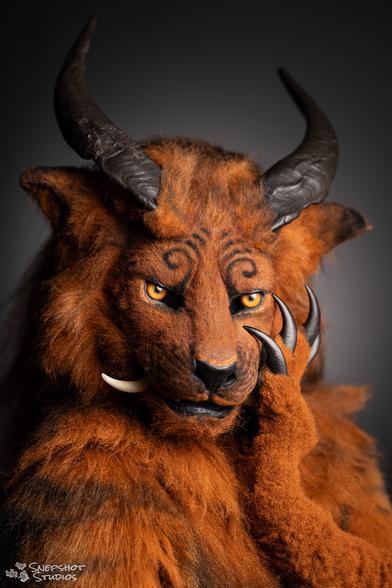 Headshot portrait of a Foodog fursuit with a grey background. Hand raised to the cheek and sporting long black claws.