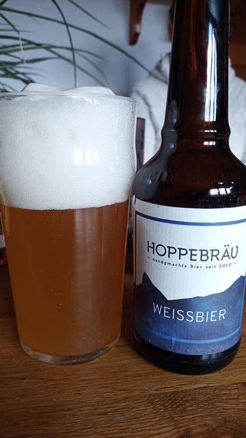 Auf einem Tisch steht ein mit trüben gelebn Bier gefülltes Glas und daneben eine kleine Bierflasche