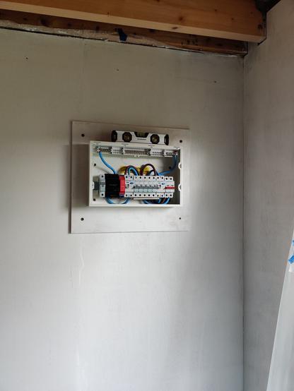 white wall with an open consumer unit (fuse box) fixed to it.