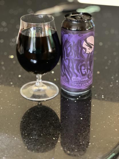 A snifter of dark beer, dark as night, next to a purple can with stylized “Night Witch” lettering and a silhouetted bi-plane flying across a pink moon