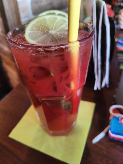 Ein rot leuchtender Raspberry Mojito Cocktail mit Strohhalm und zwei Scheiben Zitrone