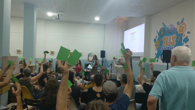 Moltes persones, la majoria assegudes, aixequen el braç per votar.