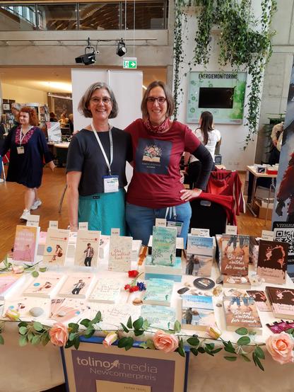 Petra Teufl (links) und Sabine Rädisch vor ihrem Messestand mit ihren Büchern